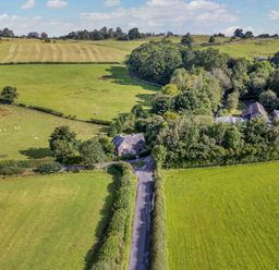 A rural landscape with green fields, a road, scattered trees, and houses surrounded by trees at Home Farm House in Penrith