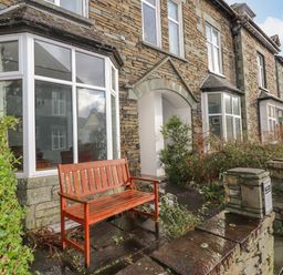 Stone terraced houses with white-framed bay windows wooden bench and small garden at Fernleigh Cottage in Ambleside