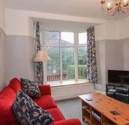 A living room with a red sofa blue floral curtains a wooden coffee table and a television at Fernleigh Cottage Ambleside