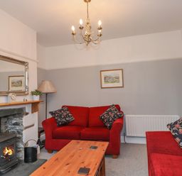A living room with red sofas a wood stove fireplace and a wooden coffee table at Fernleigh Cottage in Ambleside