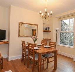 A dining area with a wooden table and four chairs next to a window and wall mirror at Fernleigh Cottage in Ambleside