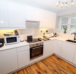 A kitchen with white cabinets a stove oven microwave and sink at Riverside Hideaway in Newby Bridge