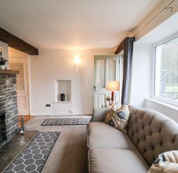 A living room with a stone fireplace a sofa with pillows a table lamp and a large window at Riverside Hideaway in Newby Bridge