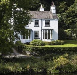A white two-story house with chimneys surrounded by trees and hedges at Loughrigg Cottage in Ambleside