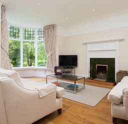 A living room with sofas a fireplace a television and large bay windows at Loughrigg Cottage in Ambleside