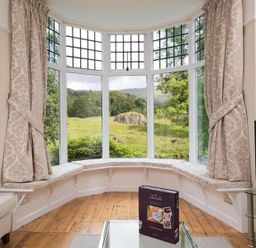 A sitting area with a bay window and curtains overlooking a green landscape at Loughrigg Cottage in Ambleside