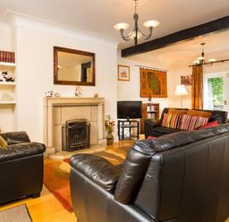 A living room with black leather sofas a fireplace a TV on a stand and orange curtains at Priory Lodge in Windermere