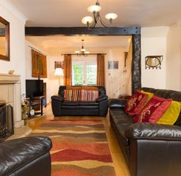 A living room with black leather sofas a fireplace a patterned rug a television a lamp and window with curtains at Priory Lodge in Windermere