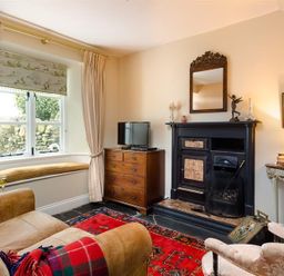 A living room with a window seat a sofa a fireplace a wooden chest of drawers and a red rug at The Blithe Hare in Troutbeck Bridge