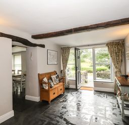 A hallway with a wooden bench and a console table next to an open door with large windows at The Mews in Ambleside