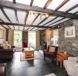 A living room with stone walls wooden beams leather and upholstered chairs and a wooden coffee table at The Mews in Ambleside