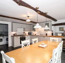 A kitchen with wooden dining table white chairs grey cabinets and exposed wooden beams at The Mews in Ambleside