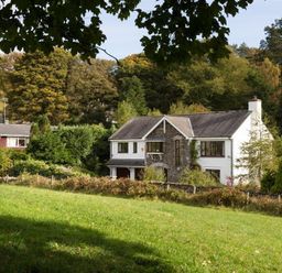 A large house with stone and white walls surrounded by trees and grass at March House in Windermere