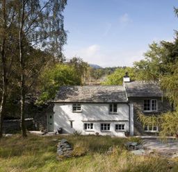 A stone and white plaster house surrounded by trees and grass at Wythebank in Langdale