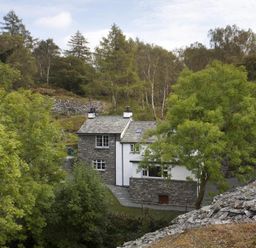 Stone and white house surrounded by trees and rocky landscape at Wythebank in Langdale