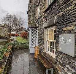 A stone building with a bench and a sign reading idle mill beside a river and a stone bridge at Idle Mill 1 in Ambleside