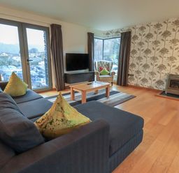 A living room with blue sofa green pillows wooden coffee table armchair and a stove at Idle Mill 1 in Ambleside