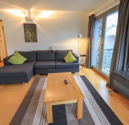 A living room with a grey sofa with green cushions a wooden coffee table and a TV at Idle Mill 1 in Ambleside