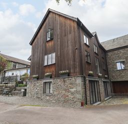 A stone and wood exterior of a multi-story house with windows and flower boxes at Le Chalet in Elterwater