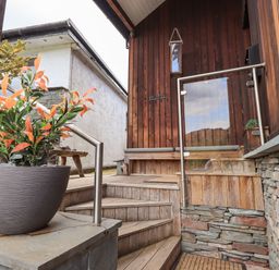 An outdoor wooden staircase with a metal railing next to a large plant in a pot at Le Chalet in Elterwater