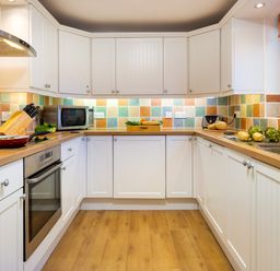A kitchen with white cabinets wooden countertops tiled backsplash and kitchen appliances at High Lake in Bowness