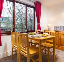 A dining area with a wooden table and chairs next to a window with red curtains at High Lake in Bowness