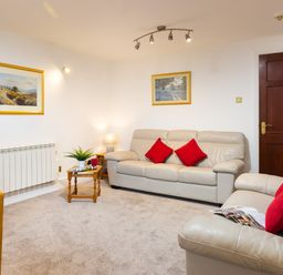 A living room with cream sofas and red cushions a wooden door and framed paintings on the walls at High Lake in Bowness