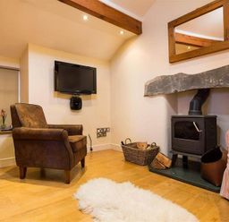 A sitting room with an armchair a wood stove and a TV mounted on the wall at Ivy Cottage in Ambleside