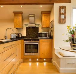 A kitchen with wooden cabinets toaster microwave oven and a small dining table with flowers and a bottle of champagne at Ivy Cottage in Ambleside