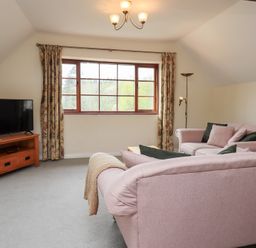 A living room with two pink sofas a wooden TV stand with a television and a large window with floral curtains at The Old Chapel in Crook