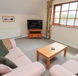 A sitting room with two pink sofas a wooden coffee table a TV on a wooden stand and a window with curtains at The Old Chapel in Crook