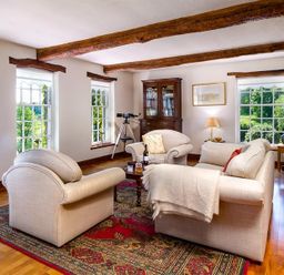 A living room with beige sofas a wooden cabinet a telescope and windows showing greenery at Bank Barn at Rusland Grizedale