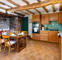 A kitchen with wooden cabinets a dining table with chairs and stone walls at Bank Barn at Rusland in Grizedale