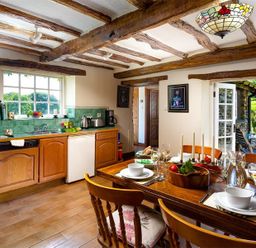 A kitchen and dining area with wooden cabinets a dining table set with tableware and a door leading outside at Bank Barn at Rusland in Grizedale