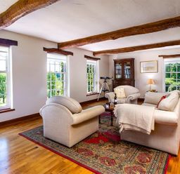 A living room with wooden beams on ceiling armchairs and a sofa around a coffee table on a rug at Bank Barn at Rusland in Grizedale