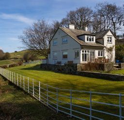 A white house with a fenced lawn and trees in the background at Juniper Cottage in Windermere