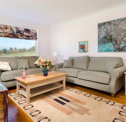 A living room with two gray sofas a wooden coffee table with flowers and wine glasses and large window at Juniper Cottage in Windermere