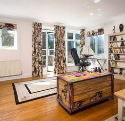A living room with wooden floors a bookshelf a black office chair and patterned curtains at Juniper Cottage in Windermere