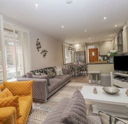 An open living room and kitchen area with sofas, a coffee table, a dining table, a television, and kitchen cabinets at Rossett Holme in Ambleside