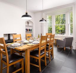 A dining room with a wooden table set for six and a gray armchair by the window at Ben House in Grasmere