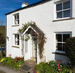 The exterior of a white house with a garden and flowers by the entrance at Birchmill Cottage in Crook