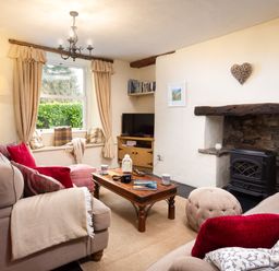A living room with sofas cushions and a coffee table by a fireplace and window at Birchmill Cottage in Crook
