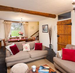 A living room with two beige sofas and red cushions next to a wooden dining table with chairs at Birchmill Cottage in Crook
