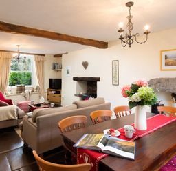 A dining table with flowers and an open book near sofas and a window in a living room at Birchmill Cottage in Crook