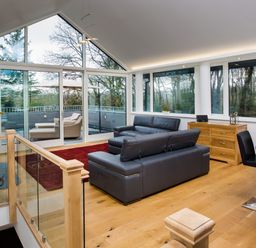 A living room with black leather sofas and large windows overlooking trees at Tall Trees in Bowness