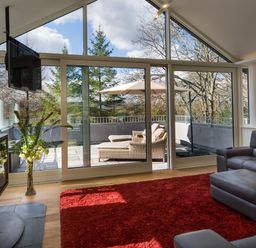 A living room with a red rug leather sofa glass sliding doors and patio furniture at Tall Trees in Bowness