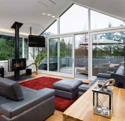 A living room with a gray sectional sofa a red rug a wood burning stove large glass doors leading to a patio at Tall Trees in Bowness