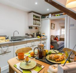 A kitchen with a wooden table set for breakfast and a couch visible through the doorway at Lettera in Ambleside