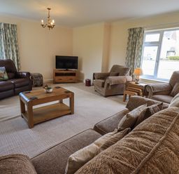 A living room with brown sofas wooden coffee table television and large windows at Laal Field House in Keswick
