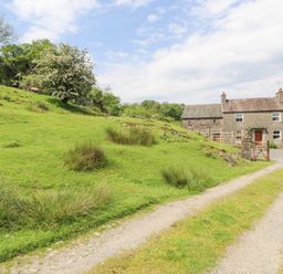 A country house with a gravel driveway and green hillside with trees and bushes at Goswick Hall in Bowland Bridge